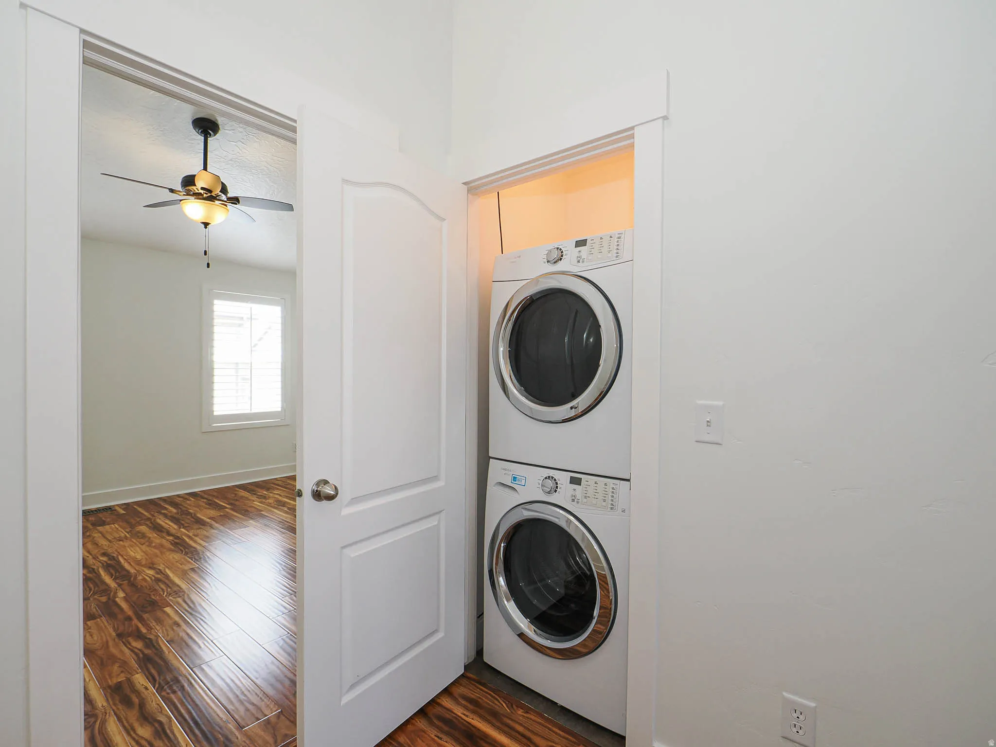 Laundry area featuring dark wood-type flooring, stacked washer / dryer, and a ceiling fan