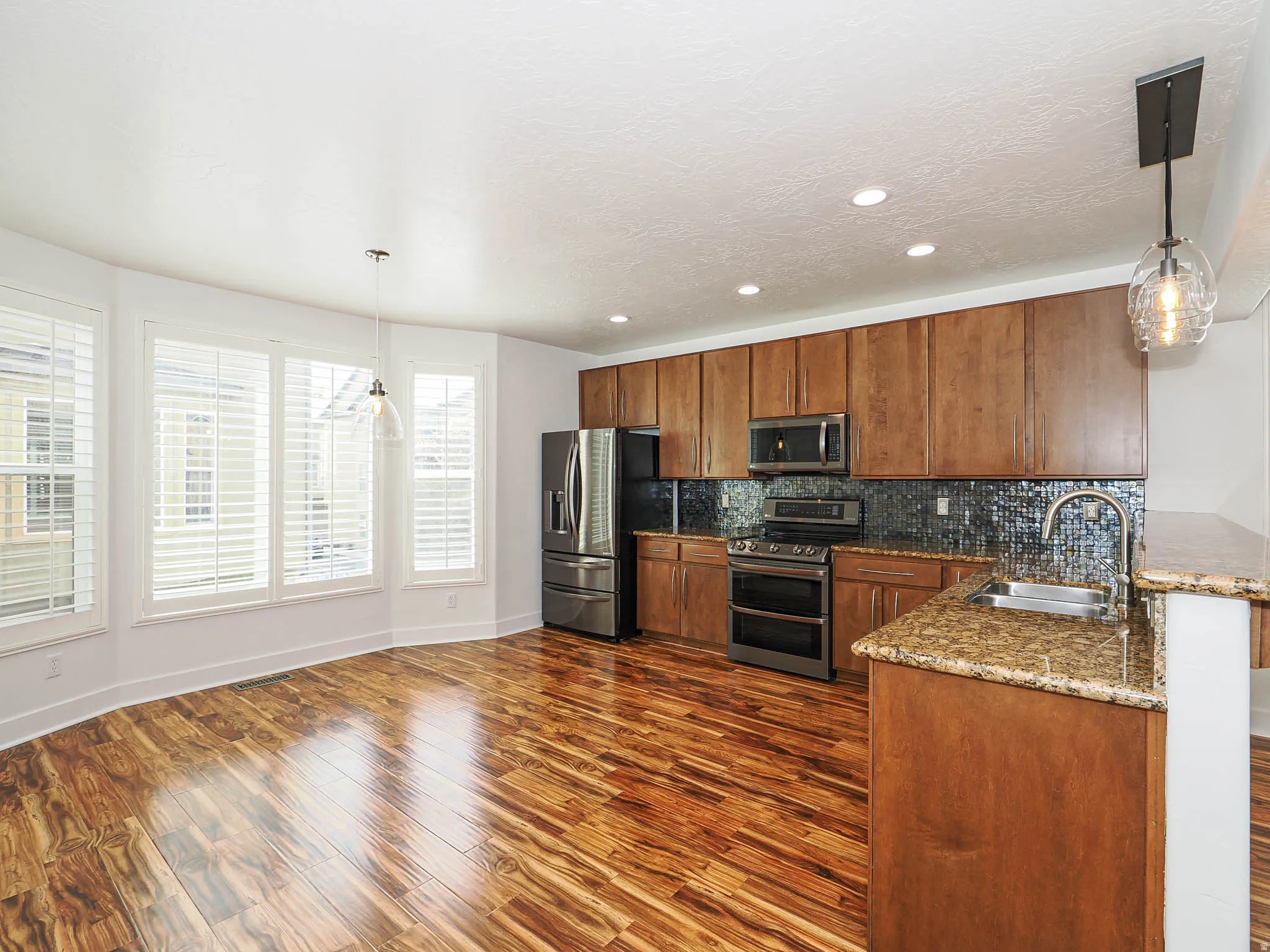 Kitchen featuring decorative light fixtures, stainless steel appliances, dark stone countertops, dark wood-type flooring, and a peninsula