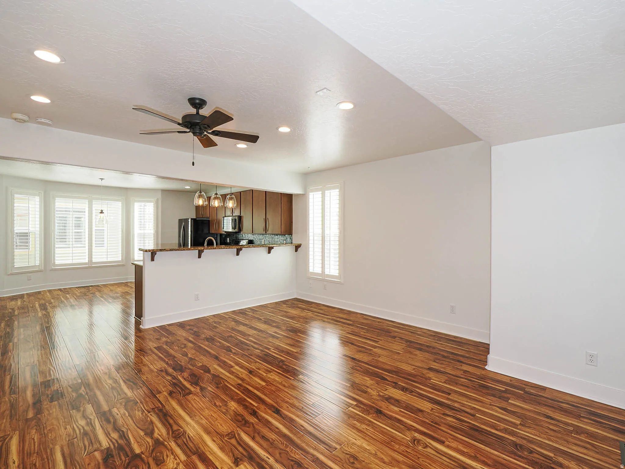 Unfurnished living room with dark wood-style floors, ceiling fan, a textured ceiling, and hanging lights