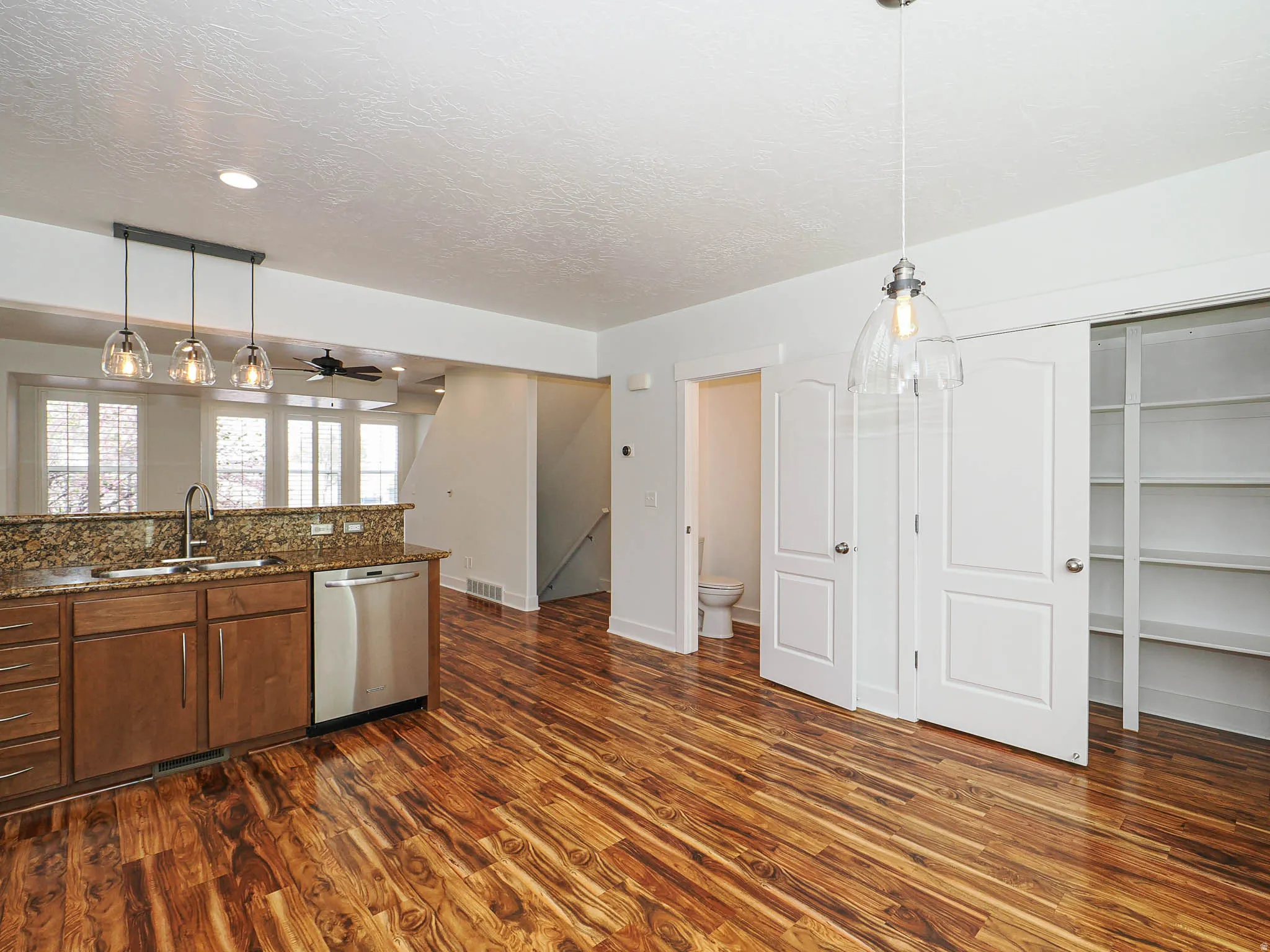 Kitchen featuring dark stone countertops, stainless steel dishwasher, pendant lighting, dark wood-type flooring, and a textured ceiling