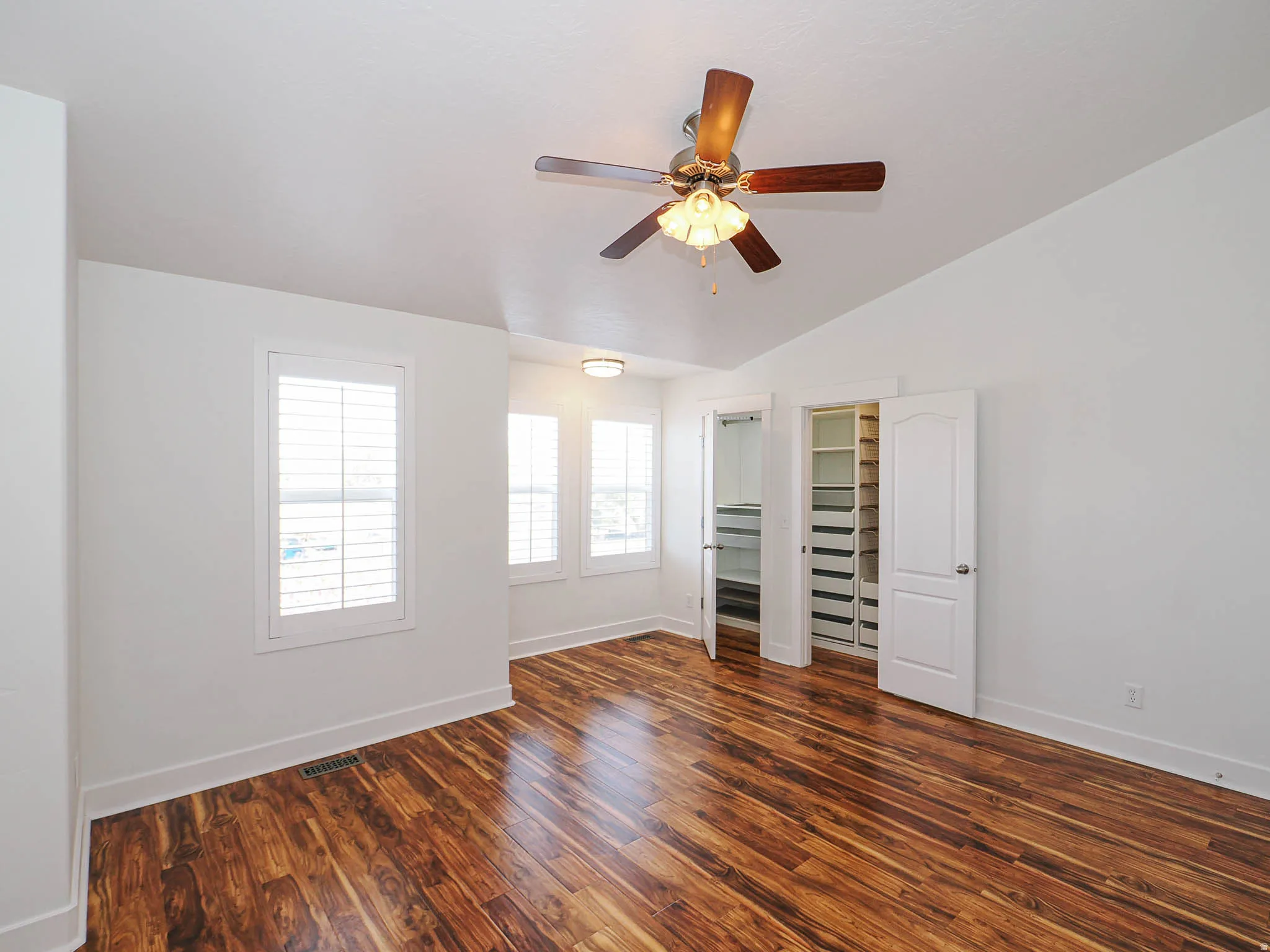 Unfurnished bedroom featuring dark wood-type flooring, ceiling fan, and lofted ceiling