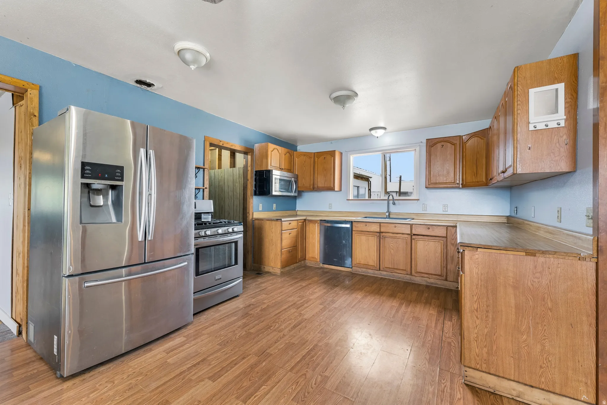 Kitchen with stainless steel appliances, light countertops, wood finish cabinets, and light wood-style flooring