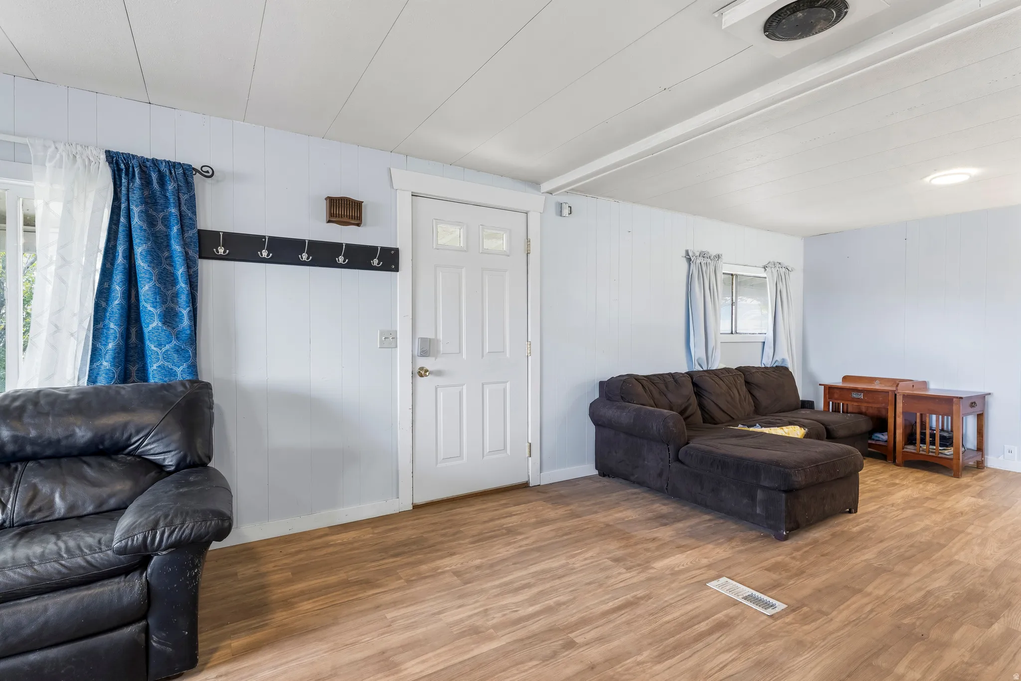 Living room with light wood-style flooring, beamed ceiling, and wooden walls
