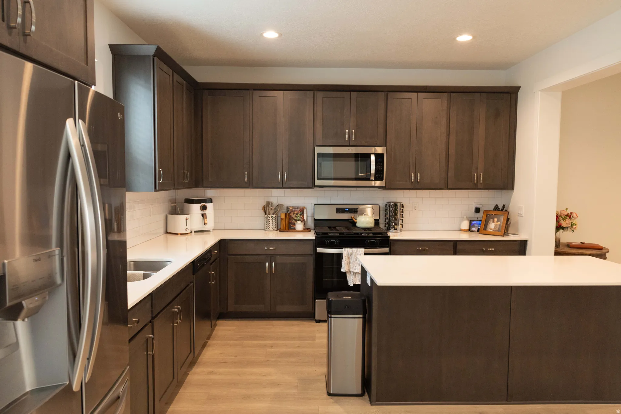 Kitchen featuring dark wood finish cabinetry, stainless steel appliances, light wood-style flooring, a kitchen island, and recessed lighting