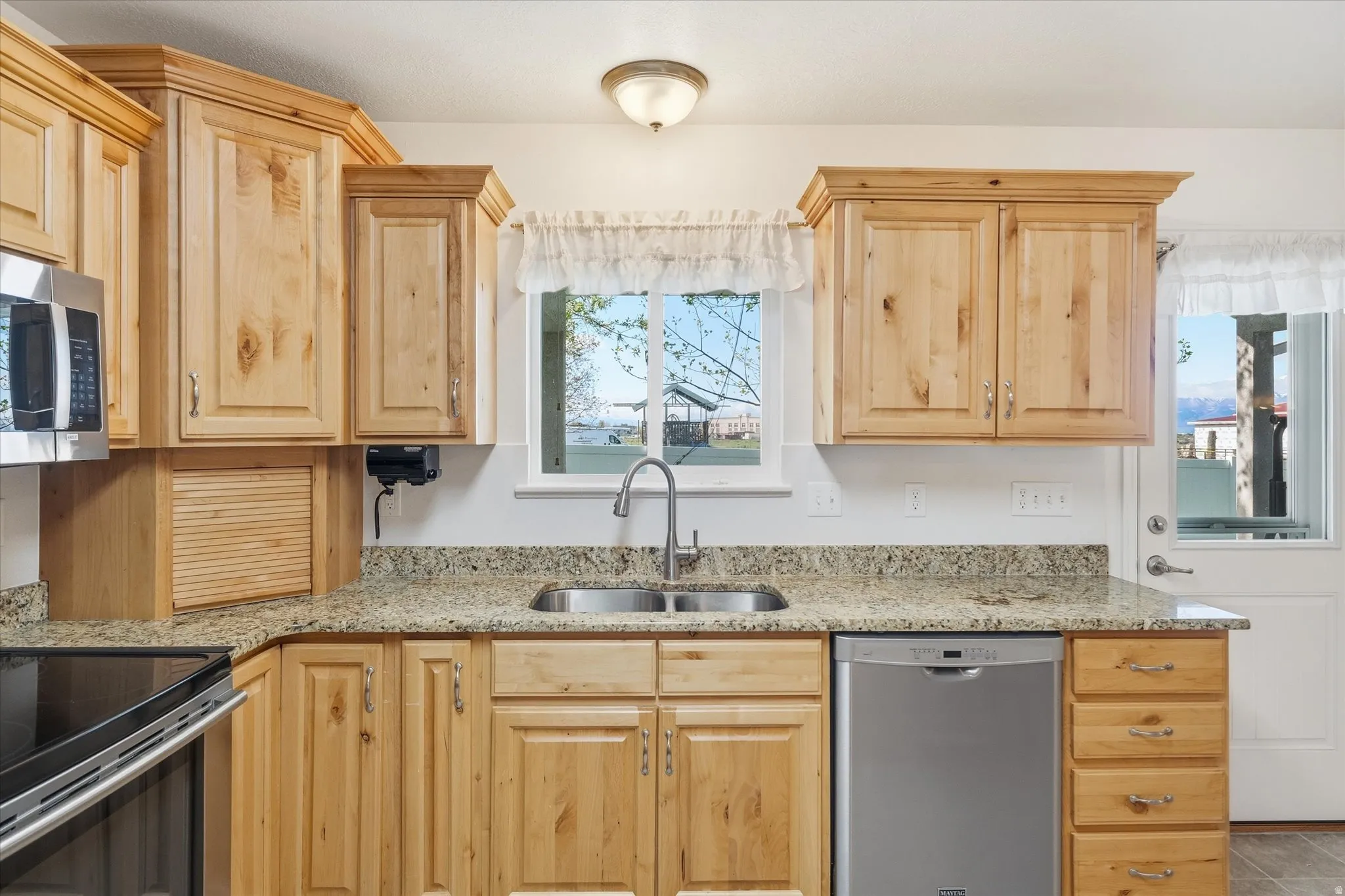 Kitchen with stainless steel appliances, light wood finish cabinets, and light stone counters