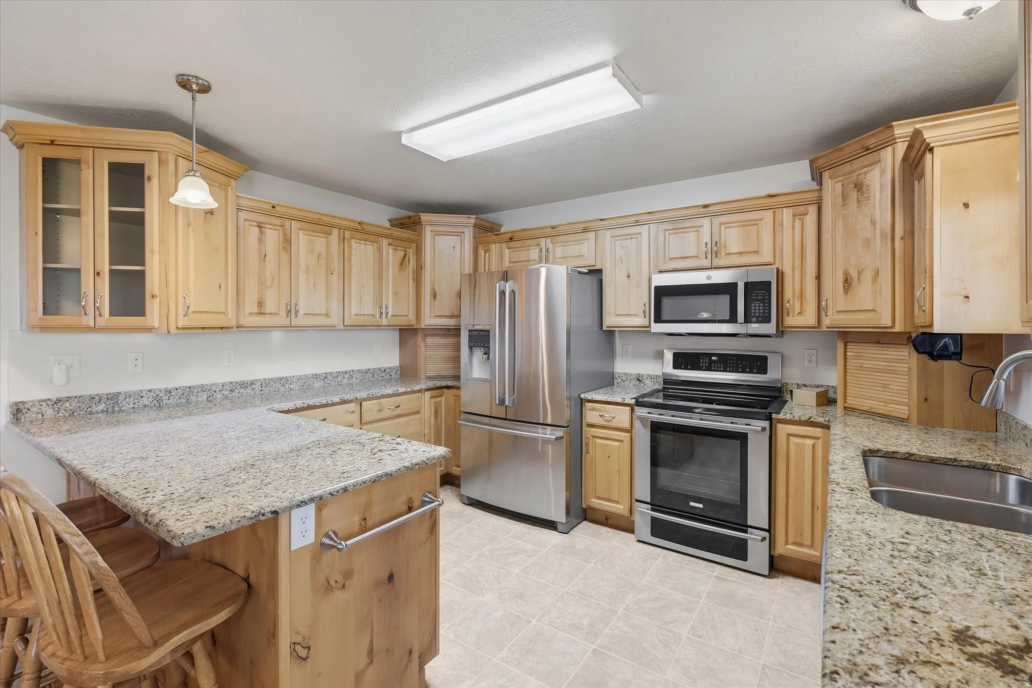 Kitchen featuring hanging light fixtures, stainless steel appliances, light stone countertops, a breakfast bar, and glass insert cabinets