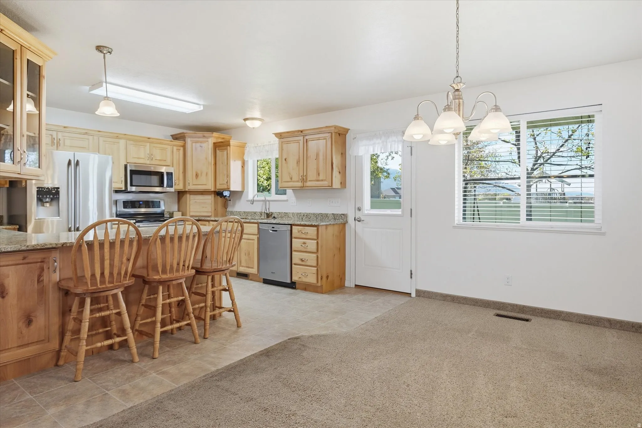 Kitchen featuring stainless steel appliances, glass fronted cabinets, a chandelier, a breakfast bar, and light carpet