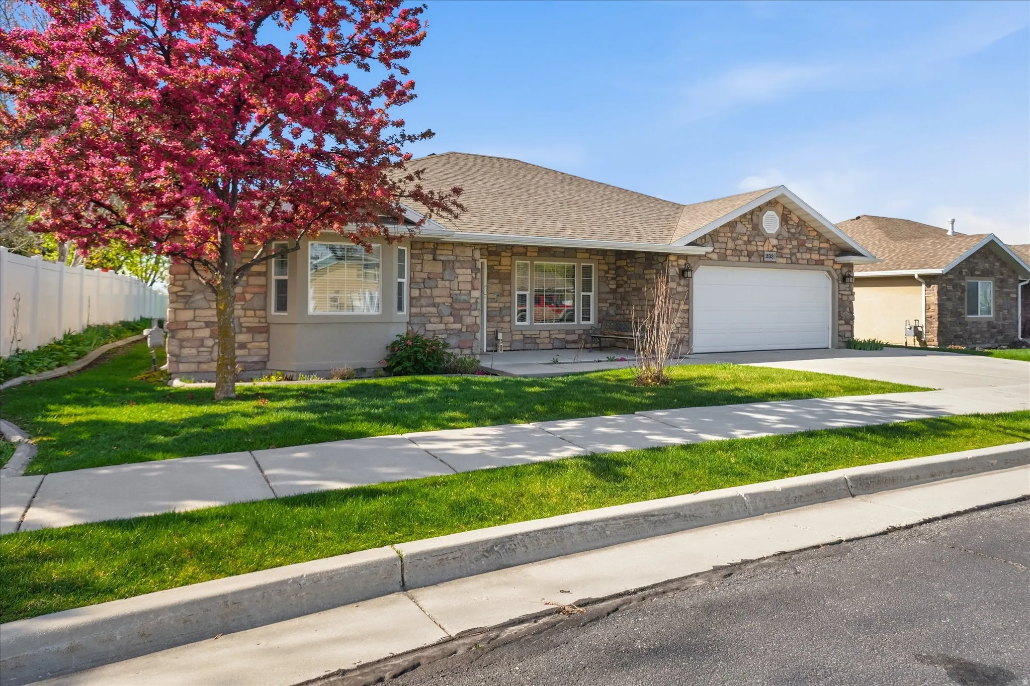 View of front of home with stone siding, a garage, a porch, driveway, and roof with shingles