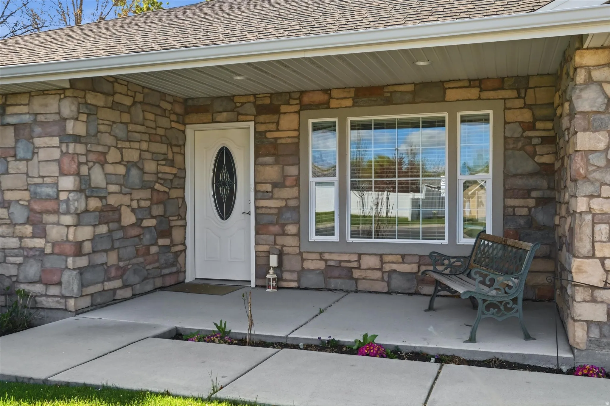 Entrance to property with stone siding, a shingled roof, and covered porch