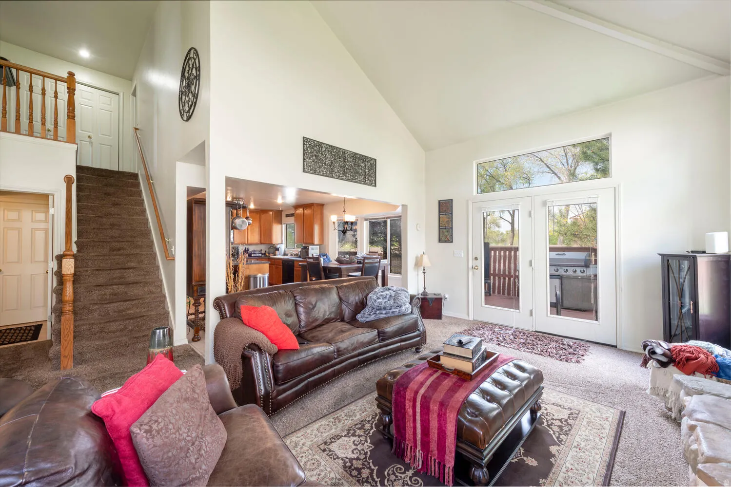Living room with a view of the outdoor deck, dining area, kitchen and staircase