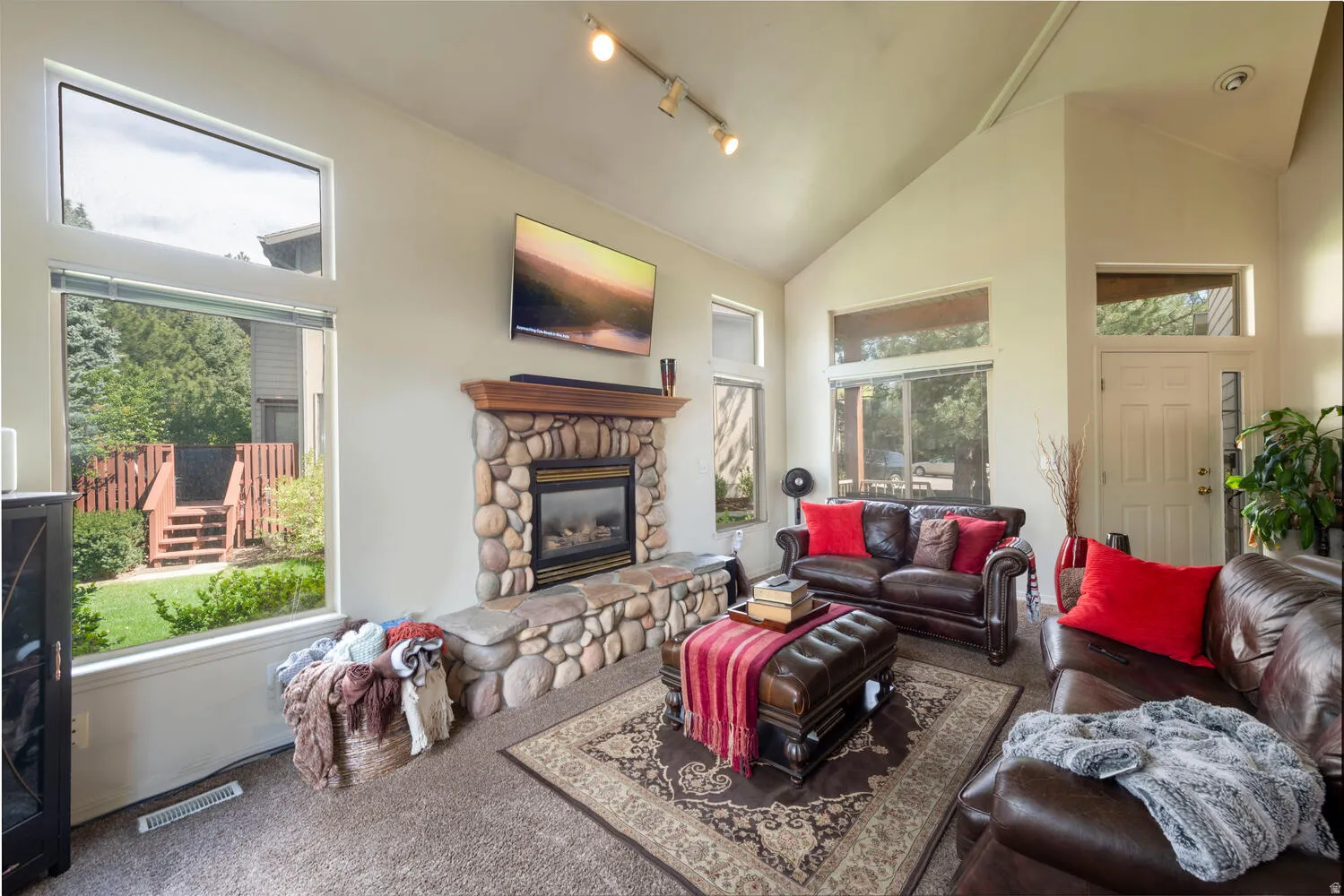 Living room with carpet floors, a fireplace, plenty of natural light, track lighting, and lofted ceiling