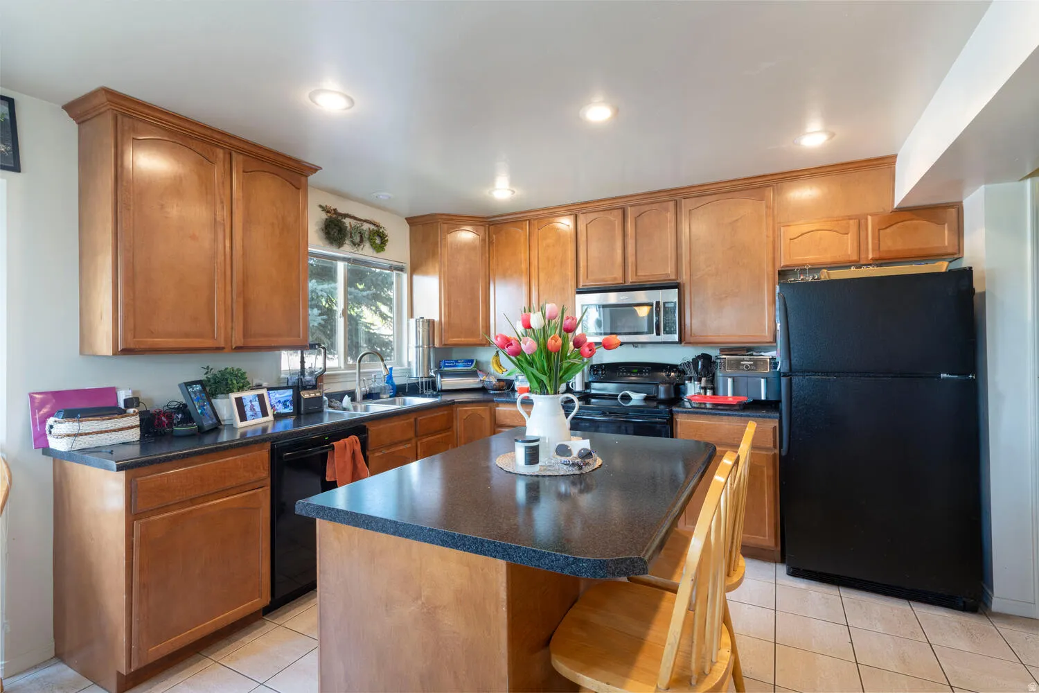 Kitchen featuring black appliances, wood finish cabinetry, a kitchen island, dark countertops, and light tile patterned flooring