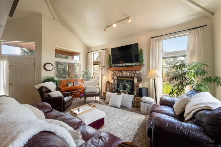 Carpeted living room with lots of natural light, a stone front fireplace and vaulted ceiling