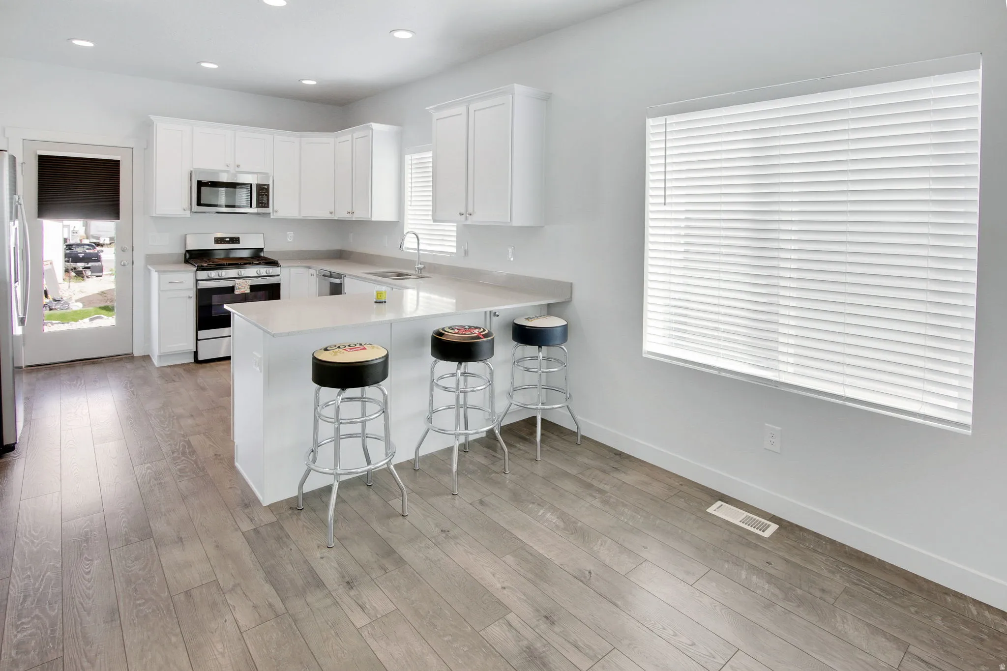 Kitchen featuring a kitchen breakfast bar, stainless steel appliances, a peninsula, white cabinetry, and recessed lighting