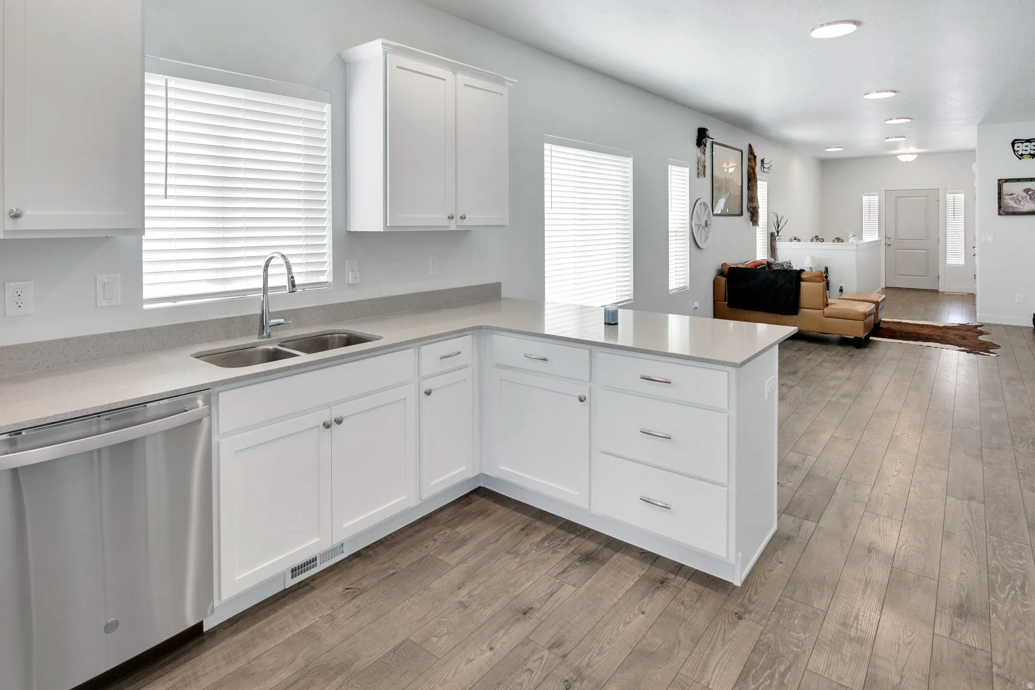 Kitchen with stainless steel dishwasher, open floor plan, light wood finished floors, white cabinetry, and recessed lighting