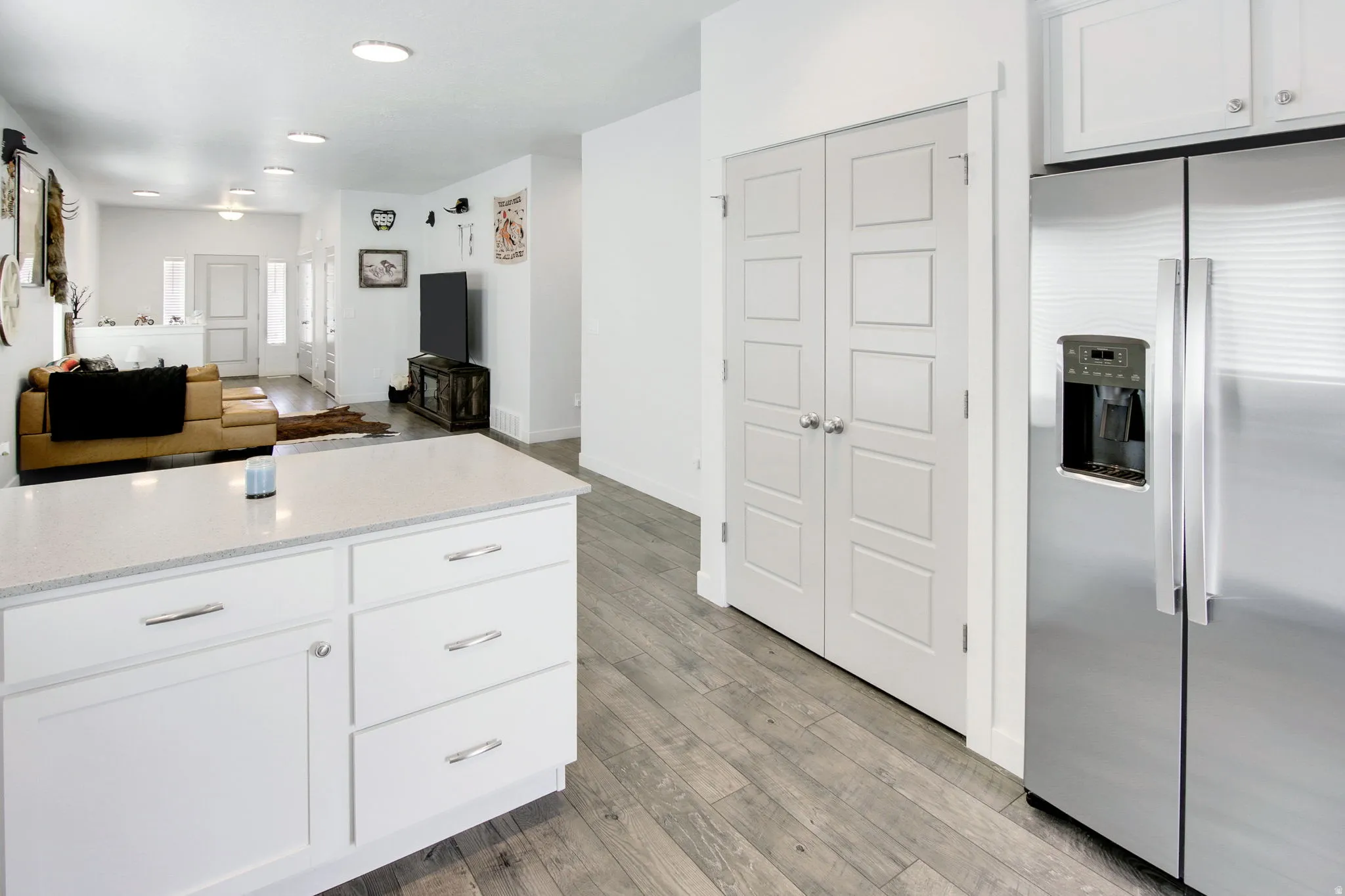 Kitchen featuring white cabinets, stainless steel fridge, light wood-style flooring, open floor plan, and light stone countertops