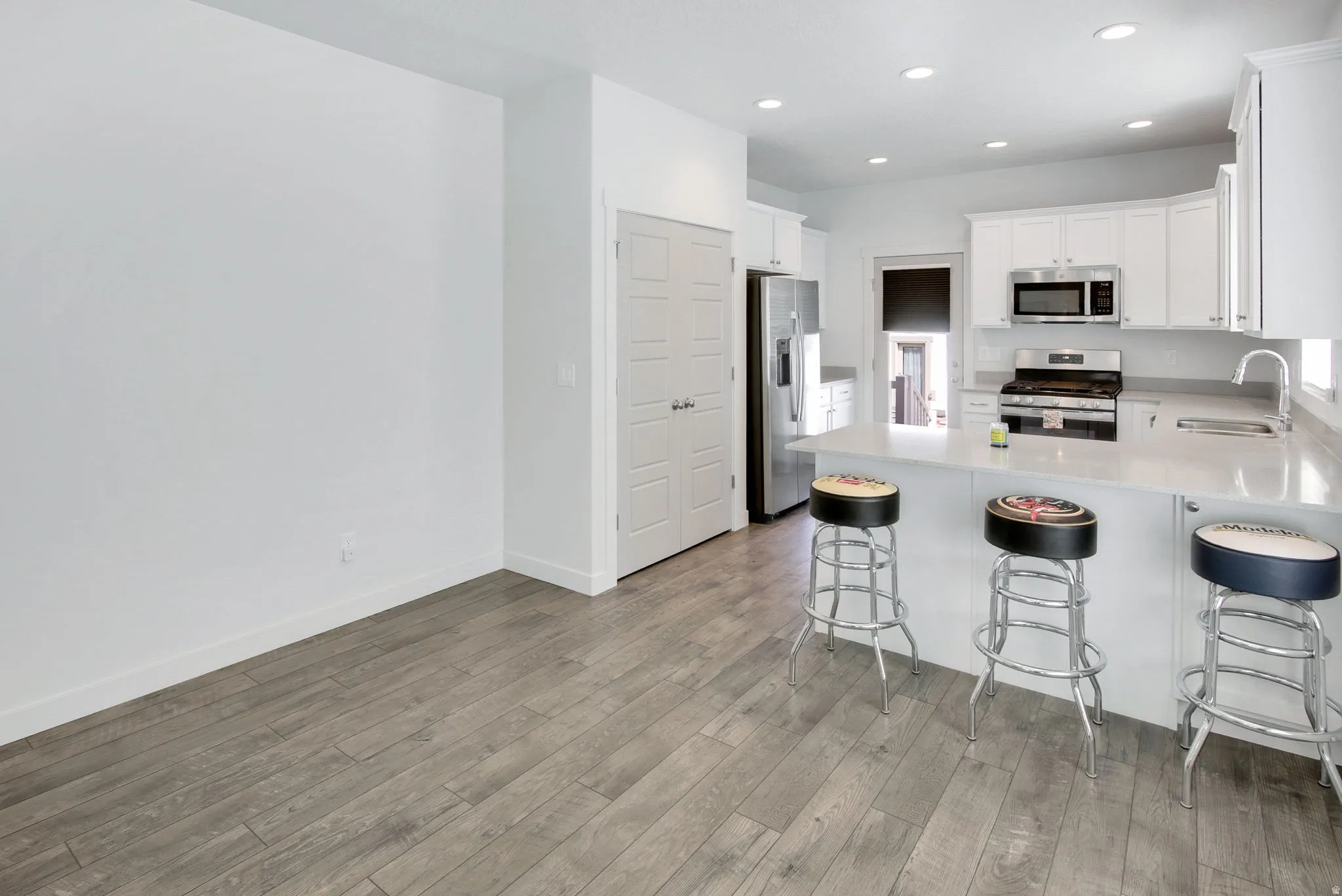 Kitchen featuring a peninsula, stainless steel appliances, white cabinetry, a kitchen breakfast bar, and light wood-style floors