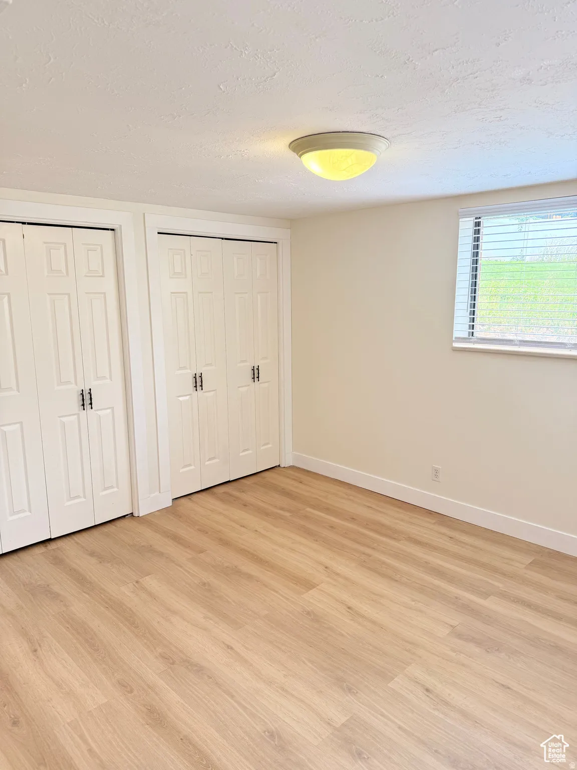 Unfurnished bedroom featuring multiple closets, a textured ceiling, and light wood-type flooring