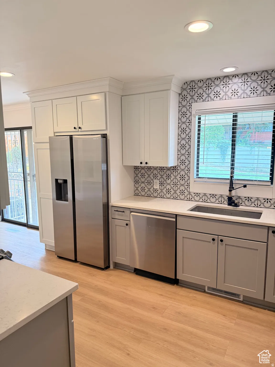 Kitchen with stainless steel appliances, gray cabinets, backsplash, light wood-style flooring, and light stone counters