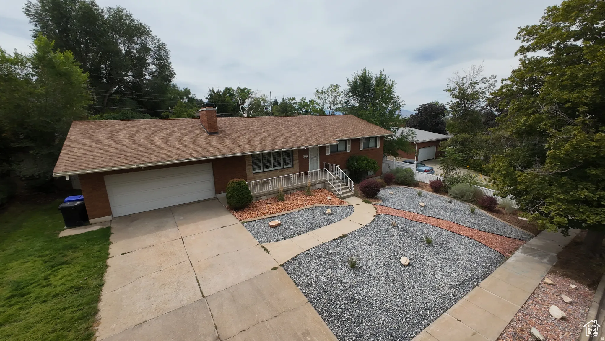 Ranch-style home with an attached garage, concrete driveway, a chimney, a porch, and roof with shingles