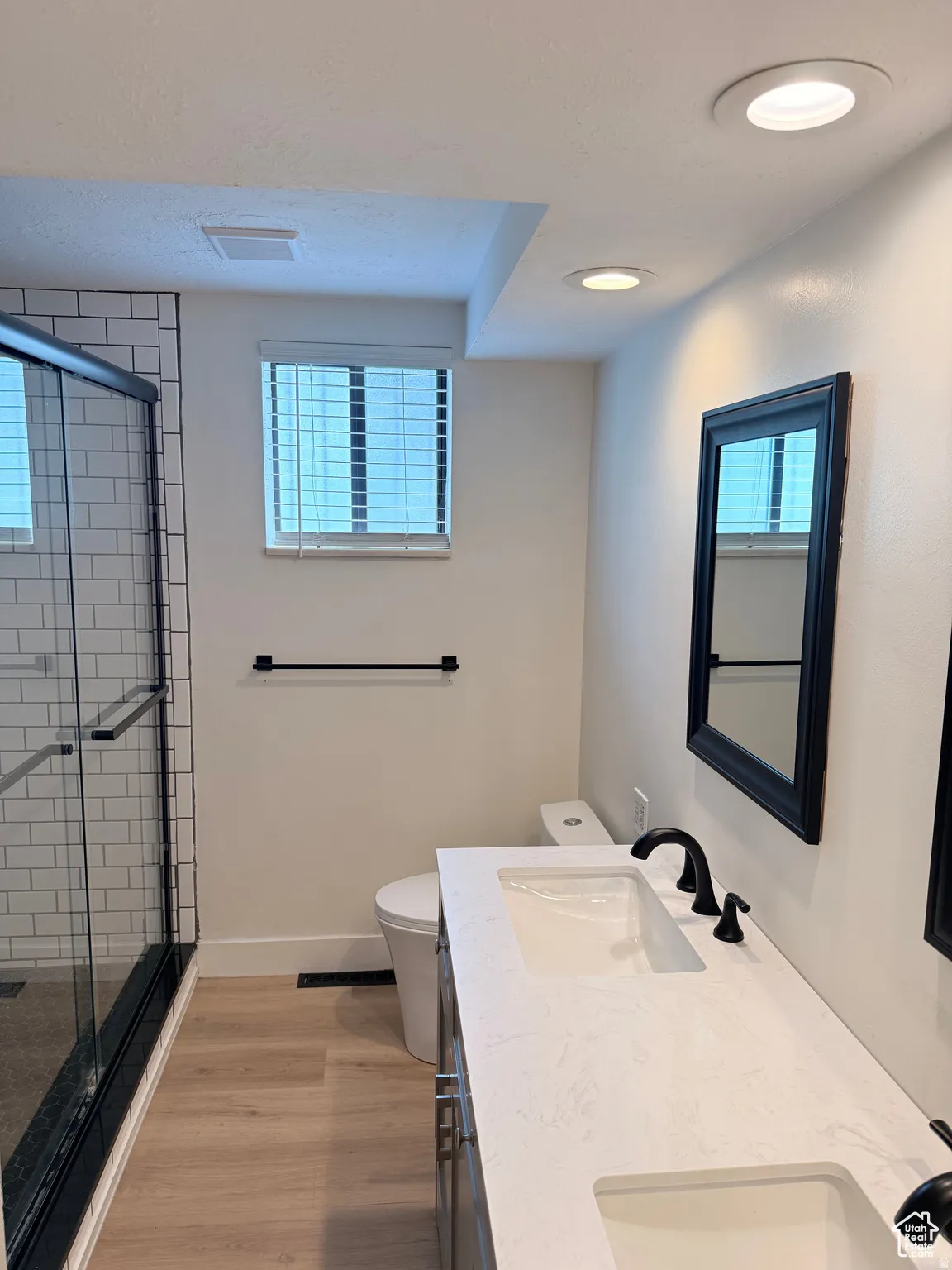 Full bath featuring double vanity, a shower stall, light wood-style flooring, and plenty of natural light
