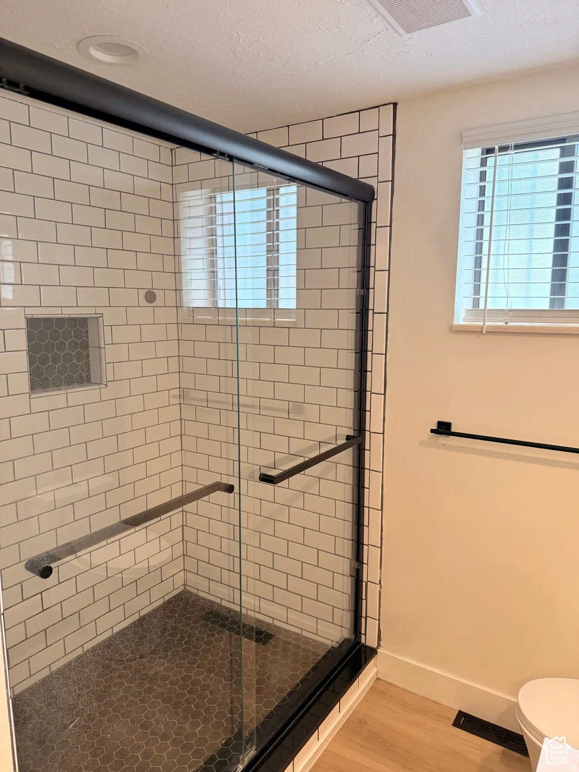 Full bath featuring a textured ceiling, a shower stall, and light wood-style floors