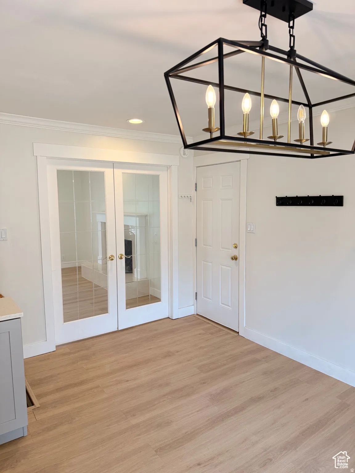 Unfurnished dining area with french doors, light wood-style flooring, ornamental molding, and a chandelier