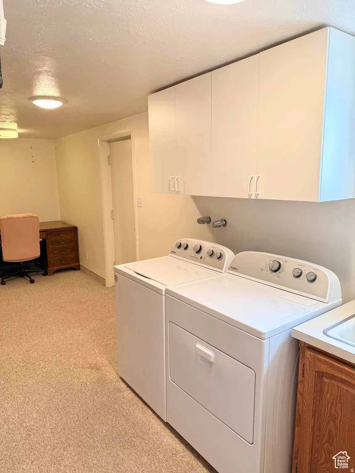 Laundry room with a textured ceiling, a desk, light carpet, washing machine and dryer, and cabinet space