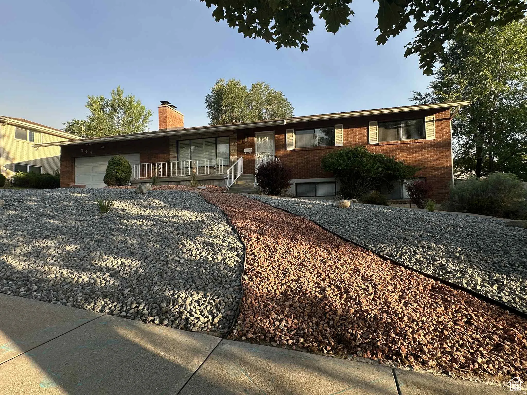 Single story home with a garage, a porch, brick siding, a chimney, and driveway