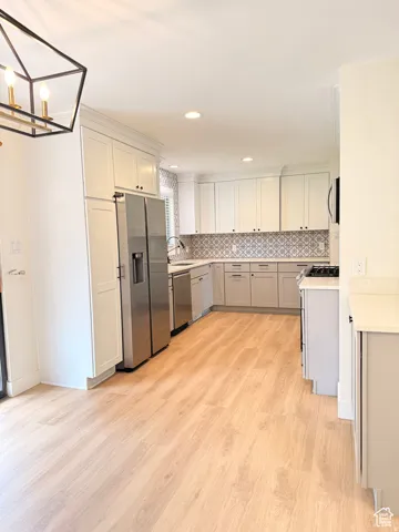 Kitchen with stainless steel appliances, light wood-style floors, tasteful backsplash, gray cabinets, and a chandelier