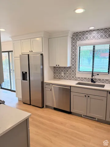 Kitchen with stainless steel appliances, gray cabinets, backsplash, light wood-style flooring, and light stone counters
