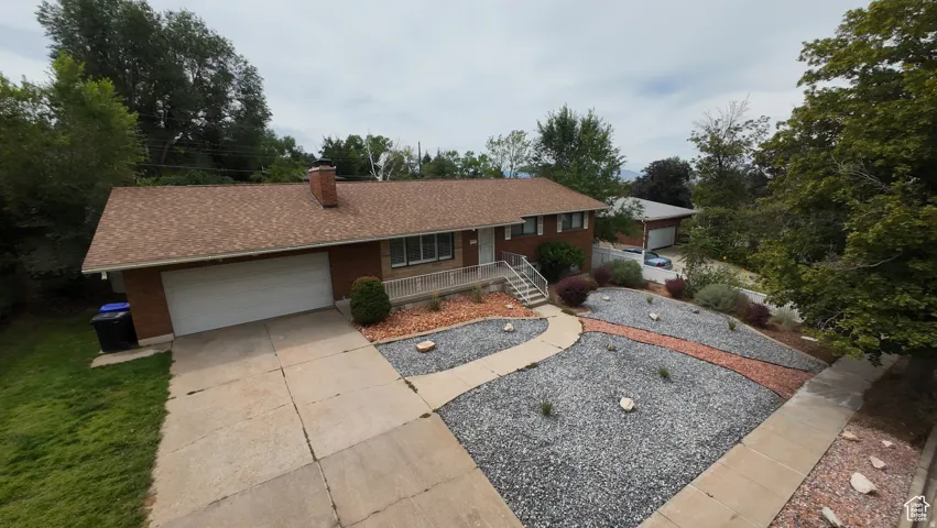 Ranch-style home with an attached garage, concrete driveway, a chimney, a porch, and roof with shingles