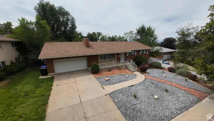 Ranch-style house with an attached garage, driveway, a chimney, a shingled roof, and brick siding