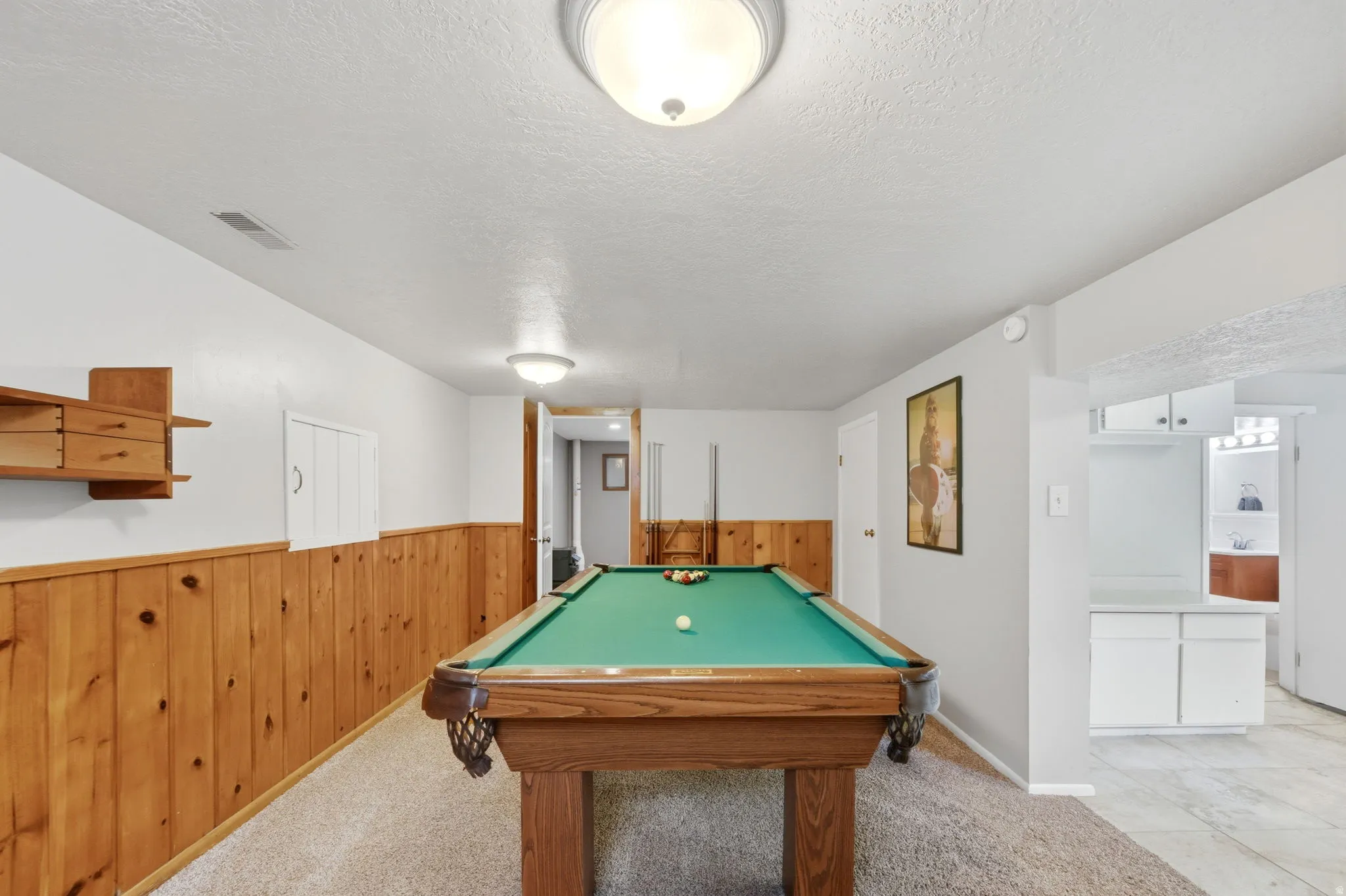 Game room with light colored carpet, a textured ceiling, billiards, wood walls, and a wainscoted wall
