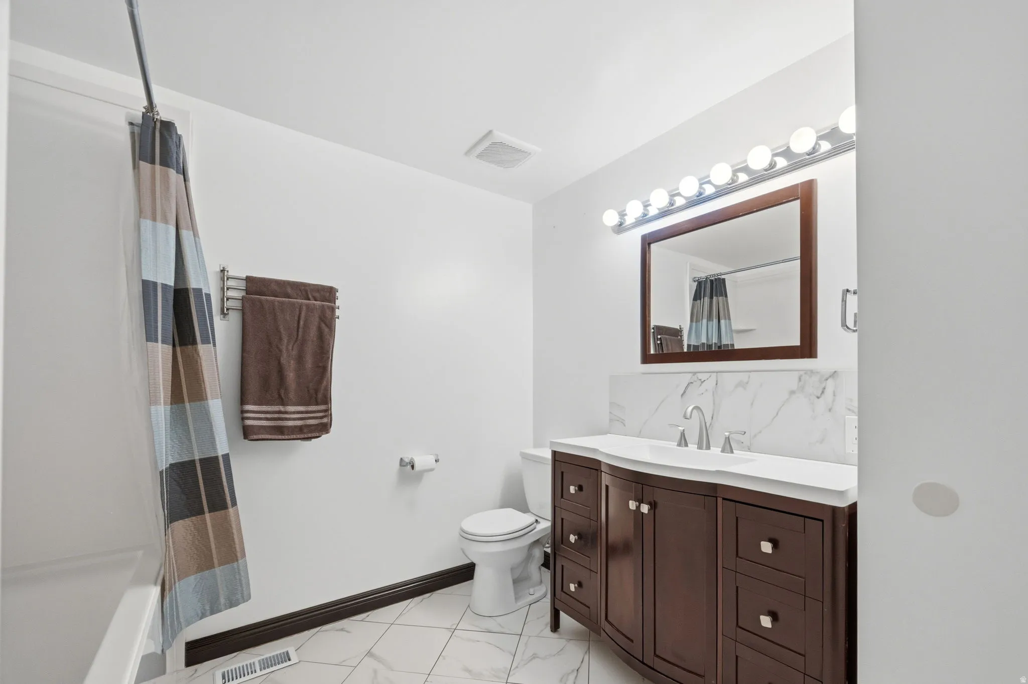 Bathroom with vanity, shower / bath combo, and light marble finish flooring
