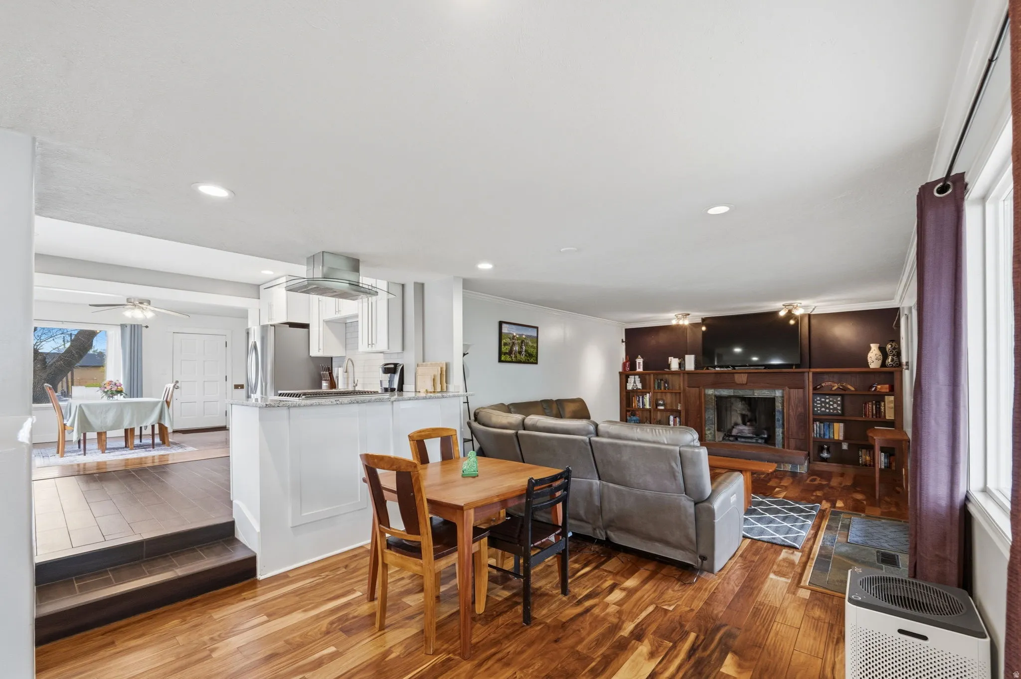 Dining space with a ceiling fan, wood finished floors, a fireplace with raised hearth, recessed lighting, and ornamental molding