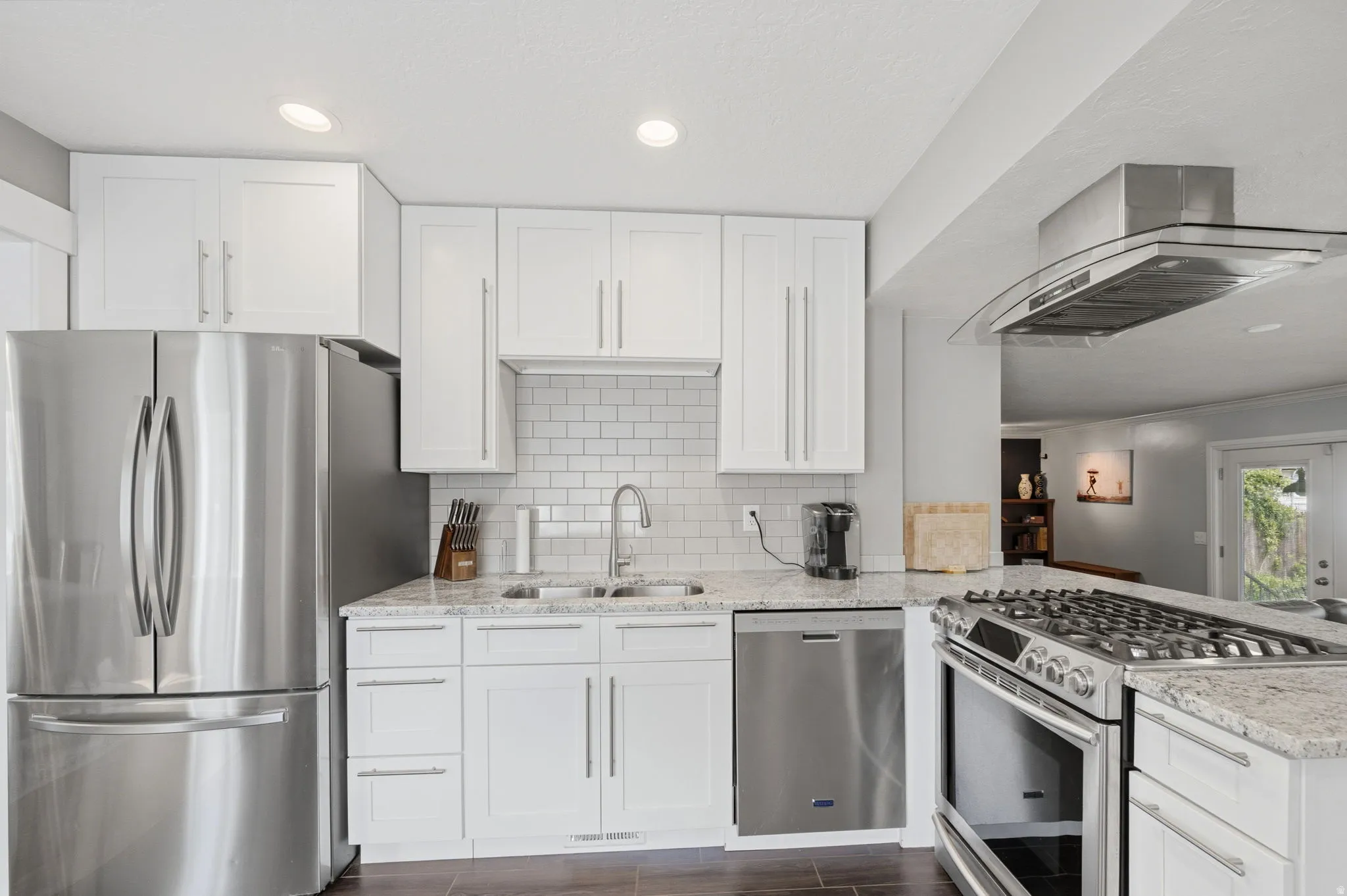 Kitchen with stainless steel appliances, light stone countertops, ventilation hood, white cabinetry, and a peninsula
