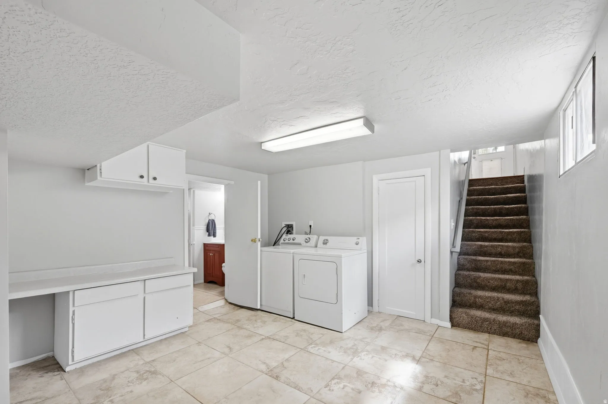 Laundry area with a textured ceiling, independent washer and dryer, and cabinet space