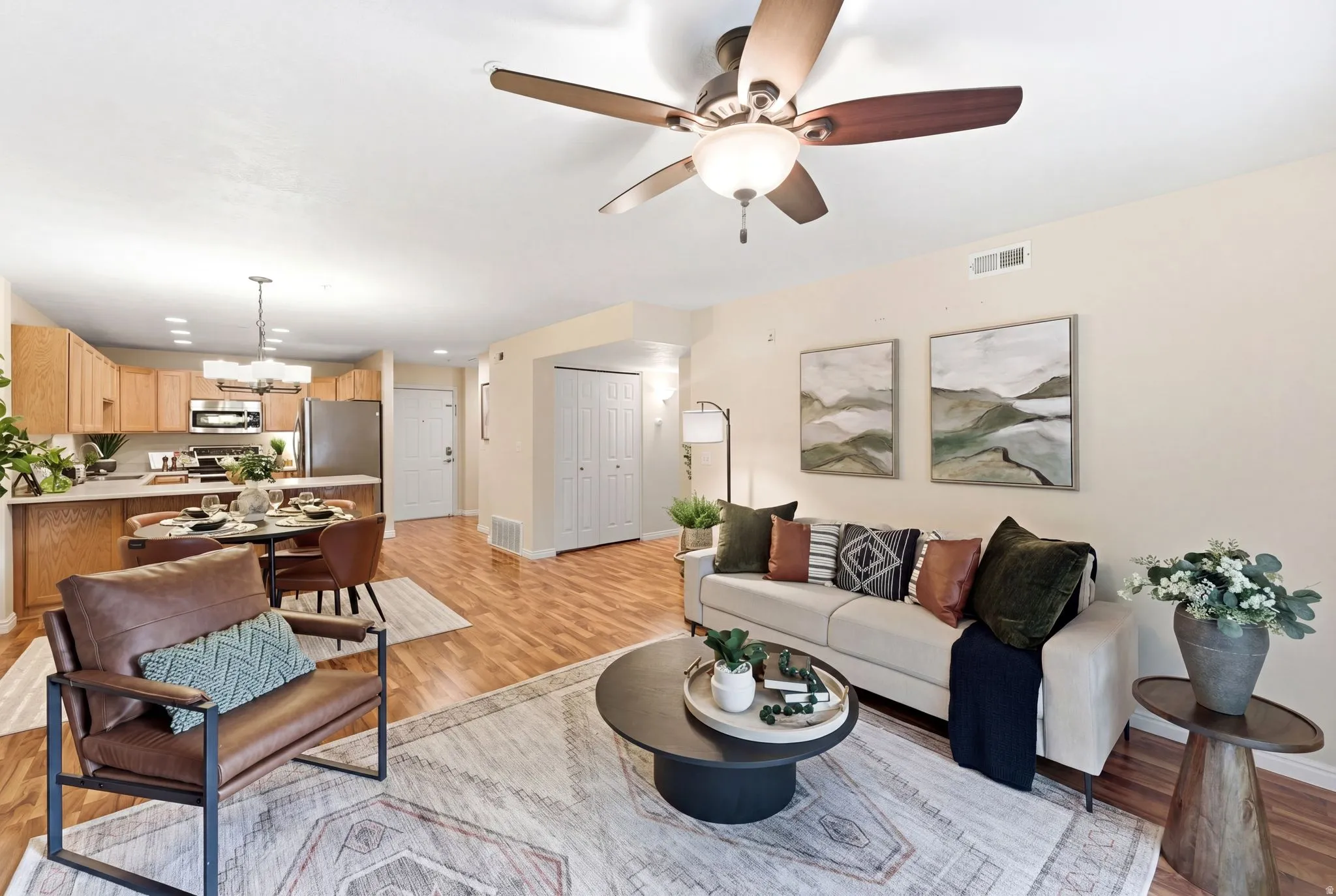 Living room featuring light wood-style flooring, suspended lighting, and a ceiling fan