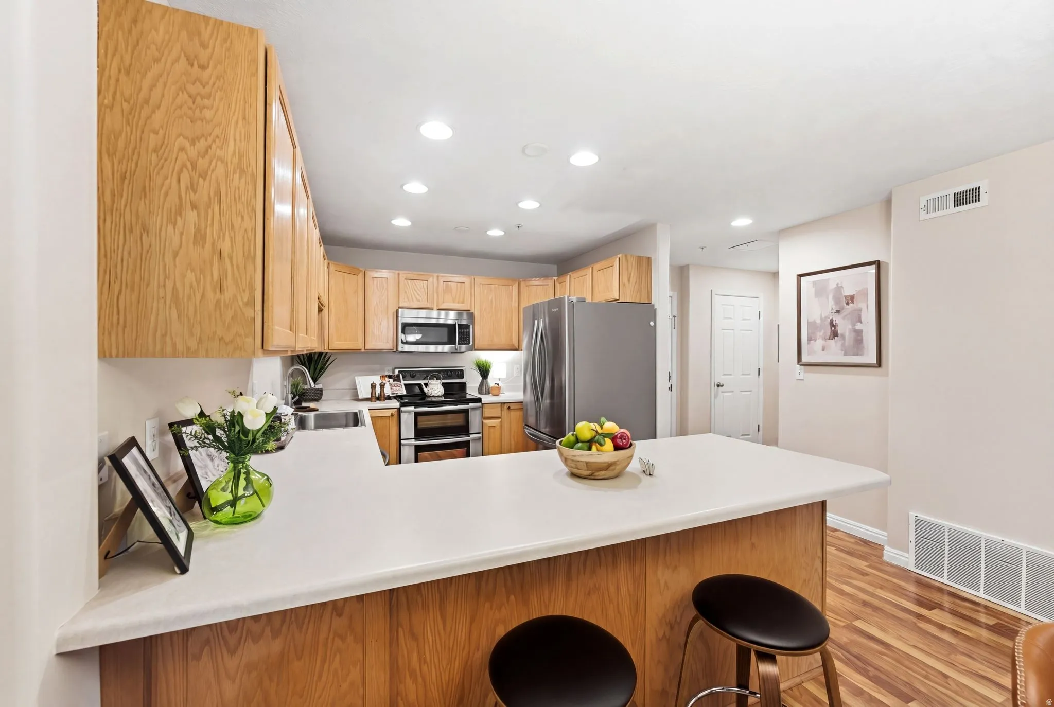 Kitchen featuring stainless steel appliances, light countertops, a kitchen bar, recessed lighting, and a peninsula