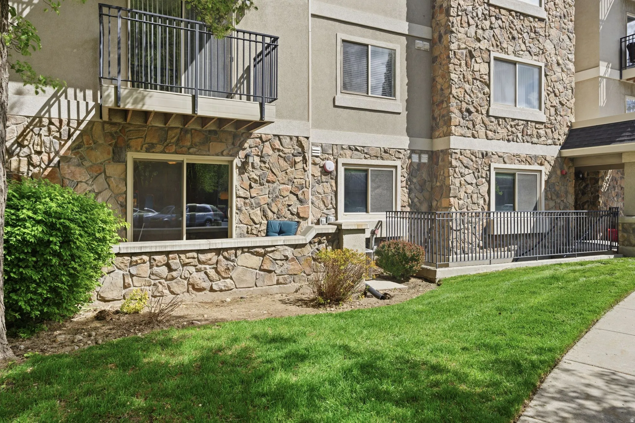 Back of house with a balcony, stone siding, a lawn, and stucco siding
