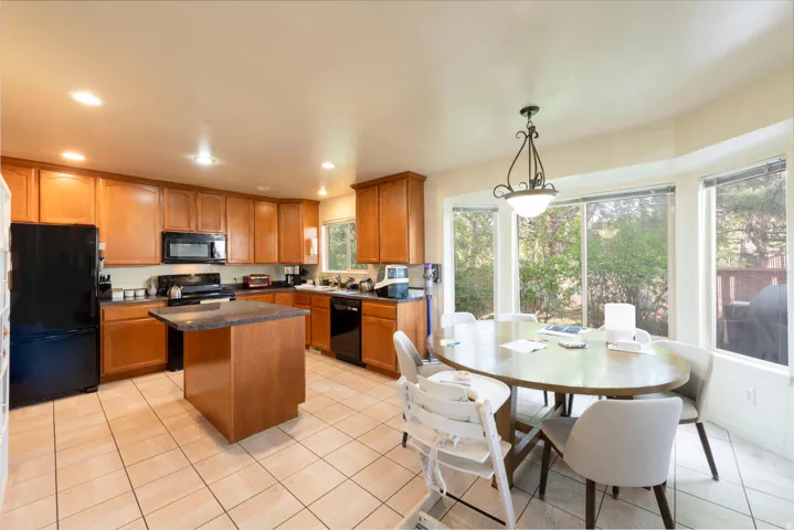 Kitchen with black appliances, wood finish cabinetry, a center island, and a bright dining area
