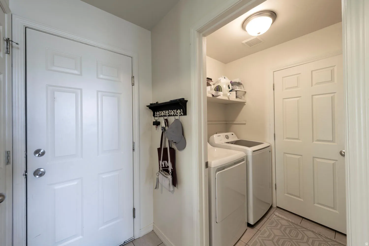 Laundry area featuring light tile patterned floors and washing machine and dryer with door to the half bath in the background