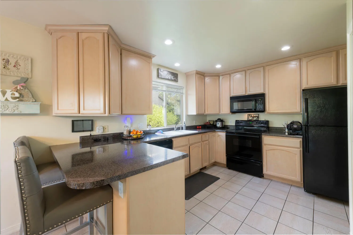 Kitchen featuring light wood finish cabinetry, black appliances, a peninsula, recessed lighting, and a kitchen bar