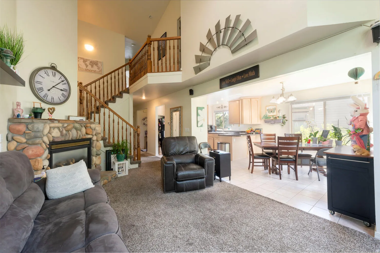Living room featuring a stone fireplace, view of the dining area and kitchen and the staircase to the upper floor
