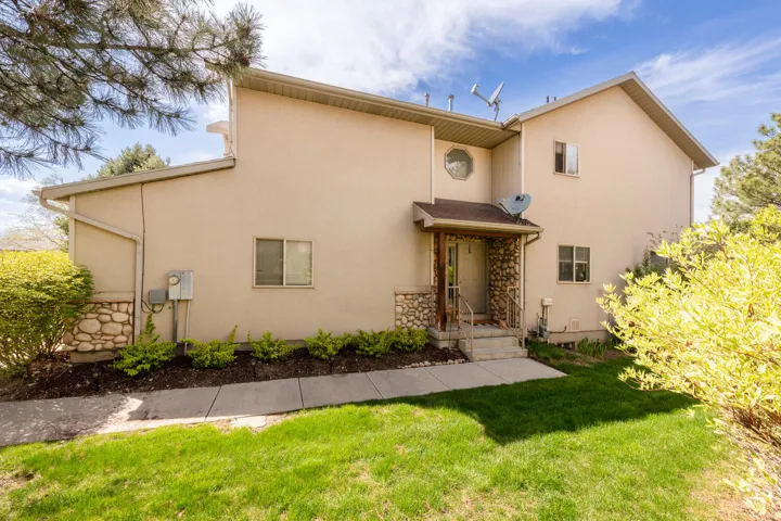 Back of property featuring a lawn, stone siding, and stucco siding