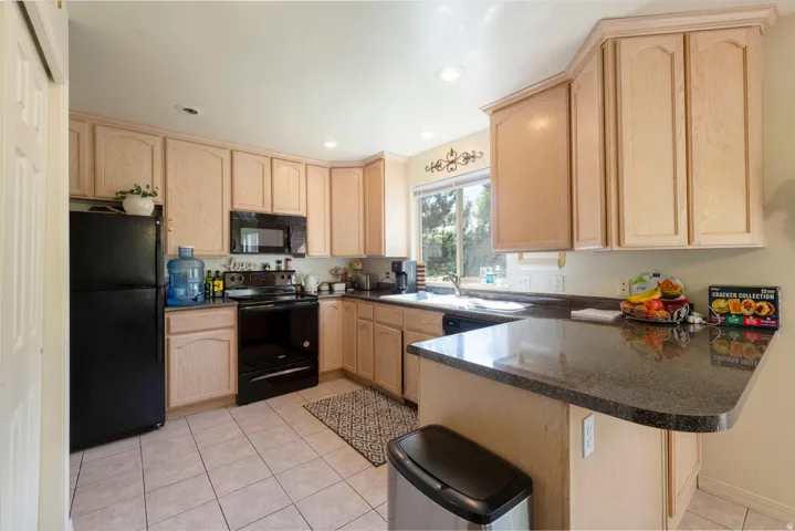Kitchen featuring light wood finish cabinets, black appliances, light tile patterned floors, a peninsula, and recessed lighting