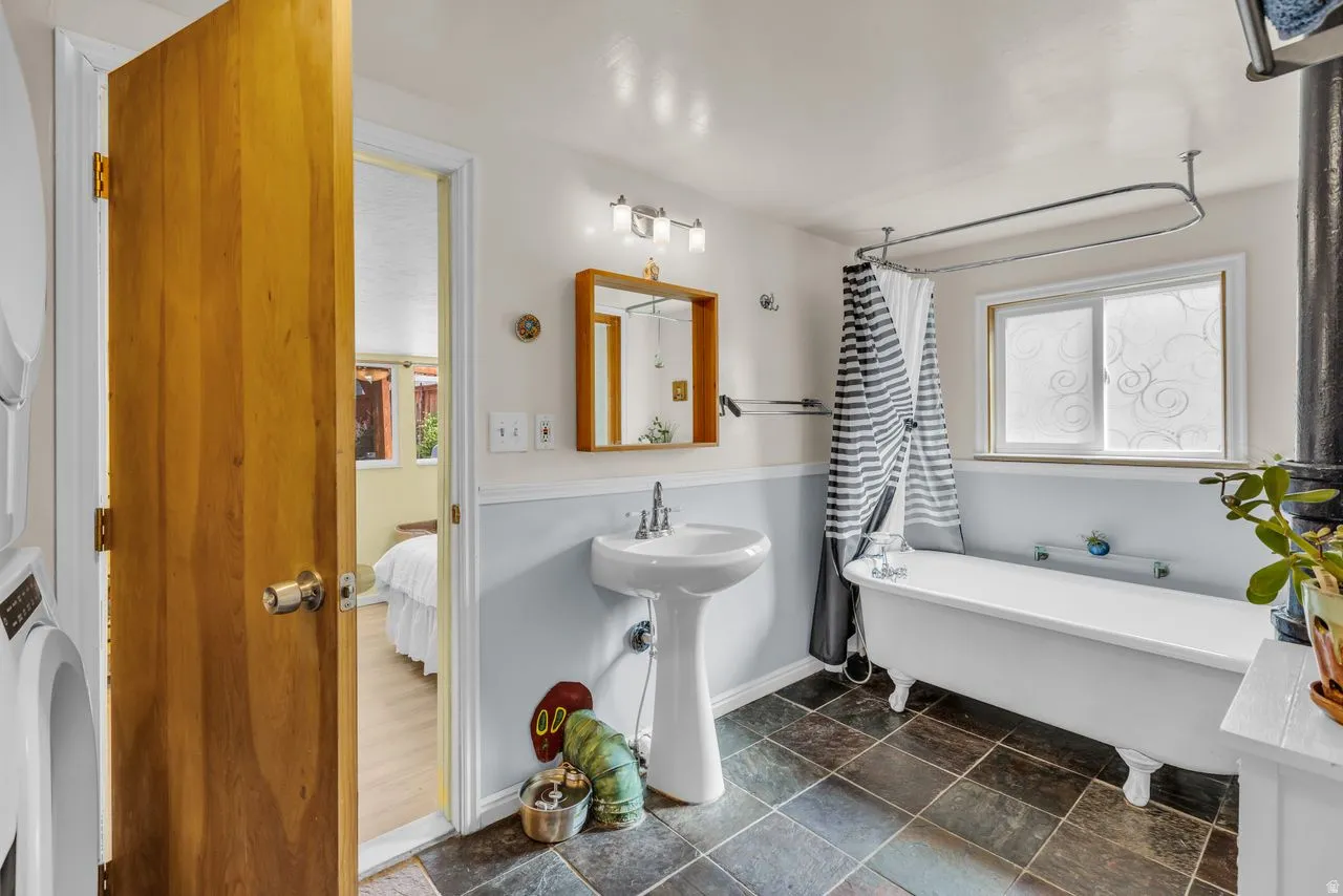 Ensuite bathroom with a soaking tub, dark stone finish flooring, washer / clothes dryer, and healthy amount of natural light