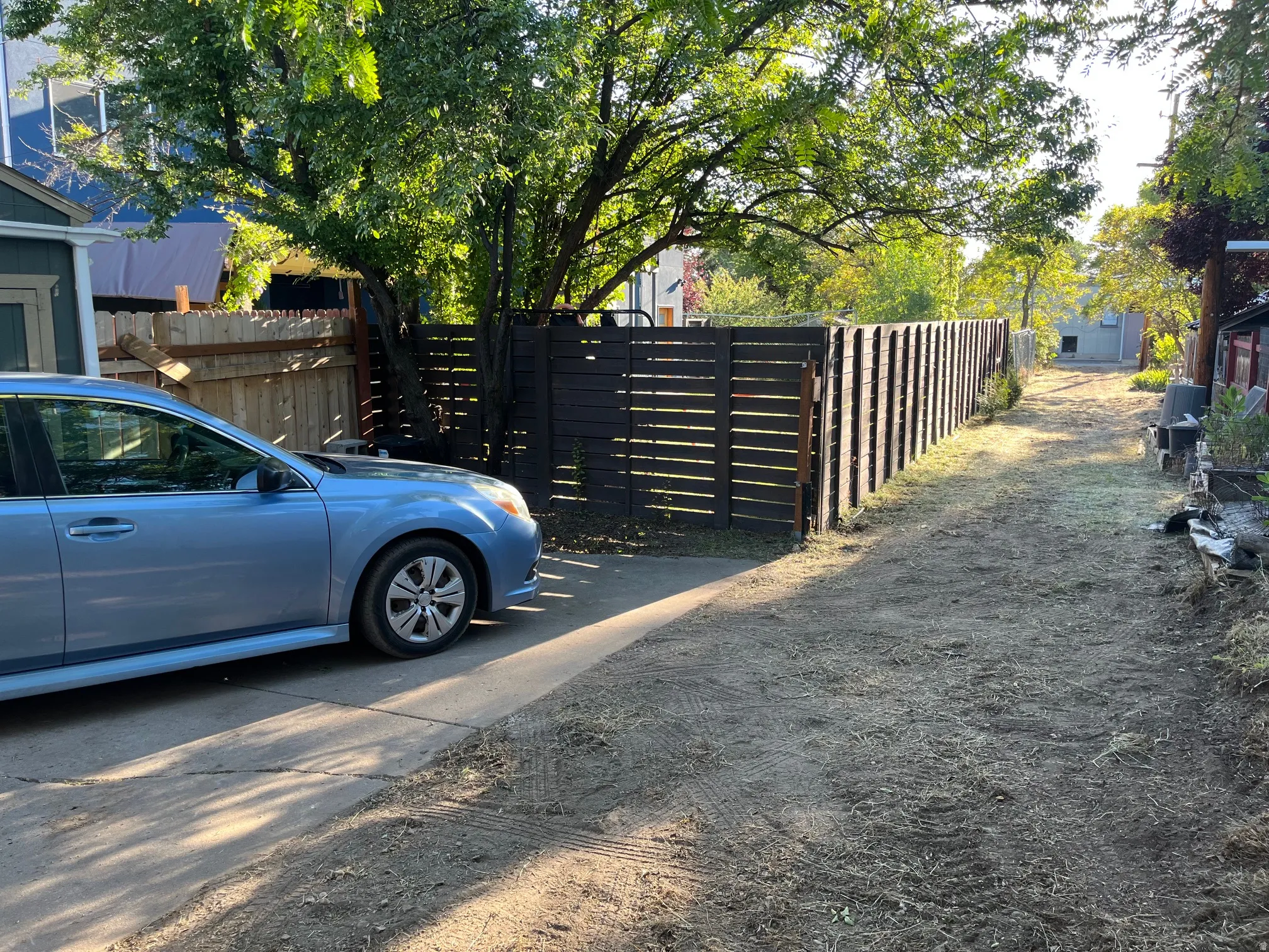 Paved driveway with a partial wooden fence and mature trees