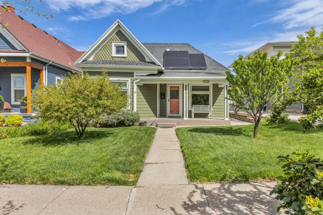 View of front of property with covered porch, roof mounted solar panels, a front lawn, and roof with shingles